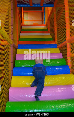 a boy in denim overalls climbs up the multi-colored stairs Stock Photo