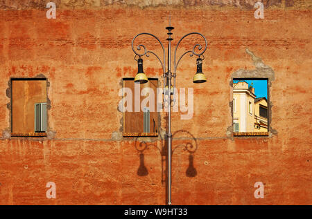 Three holes on a plain yellow wall, blue sky and windows with gray shutters. High street lamp. Rome, Italy Stock Photo