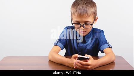 Banner Portrait of smiling boy with glasses using mobile phone on school Desk on white background. Modern mobile and communications Stock Photo