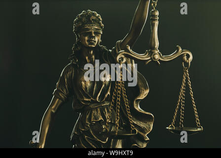 Figure of Justice wearing a blindfold holding up the scales of law over a black background in a close up conceptual view Stock Photo