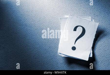 Pile of printed question marks in shaft of light on a textured grey background with copy space in a conceptual image Stock Photo