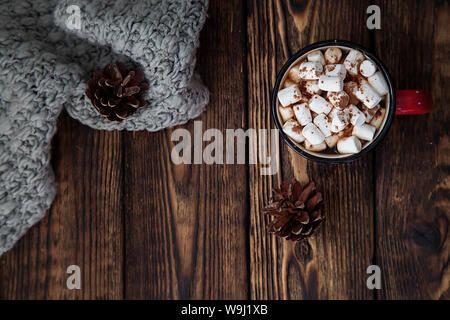 one red Cup with hot drink with marshmallow and knitted scarf on wooden christmas background Stock Photo