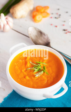 Carrot ginger cream soup with fresh ingredients on white rustic board Stock Photo
