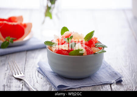 grapefruit salad with mint leaves in a bowl on a linen napkin and wooden table .Citrus diet Stock Photo