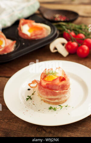 Delicious egg muffins wrapped in crispy bacon served on white plate on wooden background Stock Photo