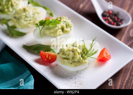 Deviled eggs with avocado puree and spices decorated with herbs and cherry tomatoes Stock Photo