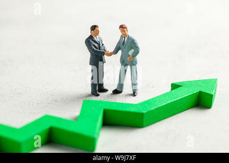 Figurine of businessmen shaking hands in suit and tie and green up arrow. The concept of success, profit growth and an increase in performance. Stock Photo