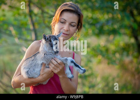 Beautiful woman with a small and nice goatling on her hands in a green background Stock Photo