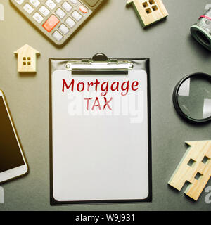 Table with wooden houses, calculator, coins, magnifying glass with the word Mortgage Tax. Property taxes. Calculation of interest on housing tax. Pena Stock Photo