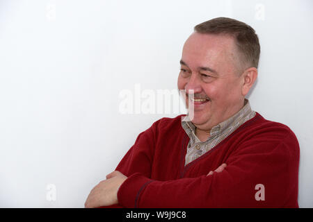 Close-up half length portrait of laughing  mature man in red pullover on white wall background. Stock Photo