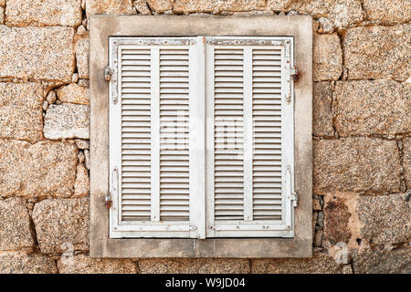 Old window with closed white wooden shutters in ancient stone wall, front view, background photo texture Stock Photo