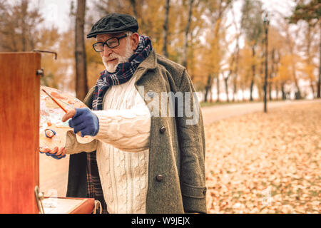 Senior man drawing a painting in park Stock Photo