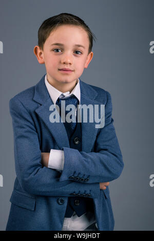 Portrait of 8 year old boy dressed in a suit for a special event or occasion like wedding or communion isolated on gray background Stock Photo