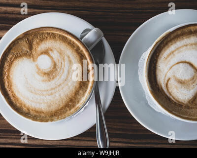 Two cups of cappuccino with latte art on wooden background. Beautiful foam, greenery ceramic cups, stylish toning, place for text. Stock Photo