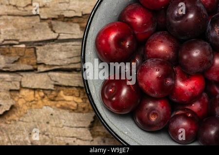 Closeup of red fresh plums in a bowl on a wooden table Stock Photo