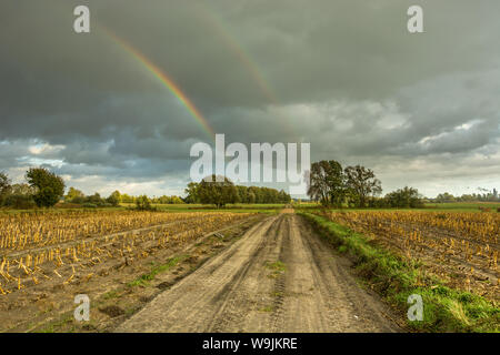 A dirt road through fields and two rainbows in the dark sky Stock Photo