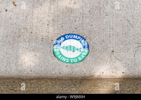 Chesapeake City, MD - May 19, 2019: Sidewalk curb above storm sewer drain with blue and green medallion with a fish on it and the words 'No Dumping Dr Stock Photo