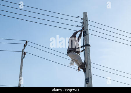 Electricty Power Lines Man Climbing. Repair Man Repair Electrical Installations. Stock Photo