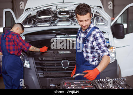 Two people working at the car repair workshop together as they fix the mechanical part of it with the help of numerous instruments. Stock Photo