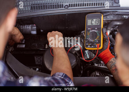 Close up of two mechanics checking the pressure in the engine of a broken car they both try to fix. Stock Photo