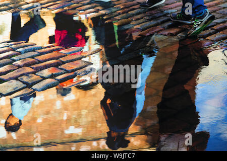 Tourists walk in the old city of Riga after the rain and are reflected in puddles on the paving of squares Stock Photo