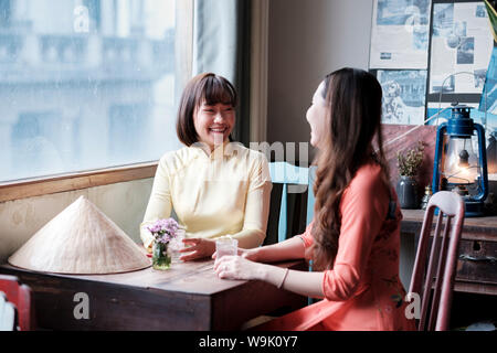 Two friends in Ao Dai dresses taking coffee in a Saigon coffee house, Ho Chi Minh City, Vietnam, Indochina, Southeast Asia, Asia Stock Photo