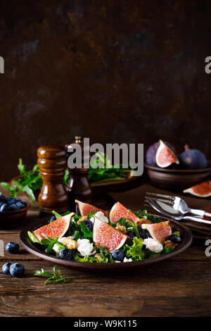 Fig salad with goat cheese, blueberry, walnuts and arugula on wooden background. Healthy food. Lunch Stock Photo