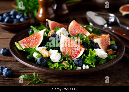 Fig salad with goat cheese, blueberry, walnuts and arugula on wooden background. Healthy food. Lunch Stock Photo