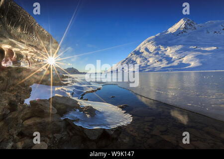 The sun shining through icicles formed on the shores of Lago Bianco at Bernina, completely frozen, Bernina Pass, Graubunden, Switzerland, Europe Stock Photo