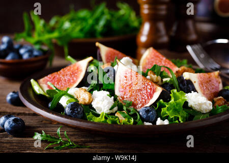 Fig salad with goat cheese, blueberry, walnuts and arugula on wooden background. Healthy food. Lunch Stock Photo