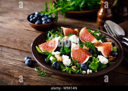 Fig salad with goat cheese, blueberry, walnuts and arugula on wooden background. Healthy food. Lunch Stock Photo