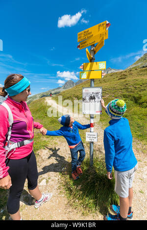 Mother and sons look at the signpost of hiking trails, Spluga Pass, Chiavenna Valley, Spluga Valley, Lombardy, Italy, Europe Stock Photo