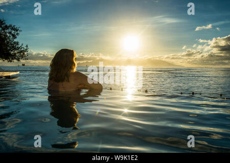 Woman enjoying the sunset in a swimming pool with Moorea in the background, Papeete, Tahiti, Society Islands, French Polynesia, Pacific Stock Photo