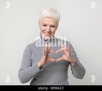 Charming aged woman showing heart gesture and smiling Stock Photo