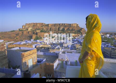 A woman in a yellow sari looking out over the 'Blue city' and fort, Jodhpur, Rajasthan State, India, Asia Stock Photo