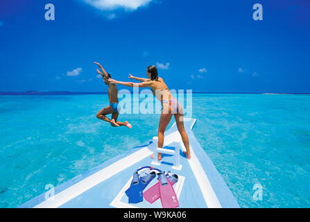 Couple at front of boat, man jumping in water, Maldives, Indian Ocean, Asia Stock Photo