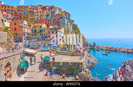 Manarola, La Spezia, Italy - July 2, 2019: Panoramic view of  waterfront with resting people in Manarola town on sunny summer day, Cinque Terre Stock Photo