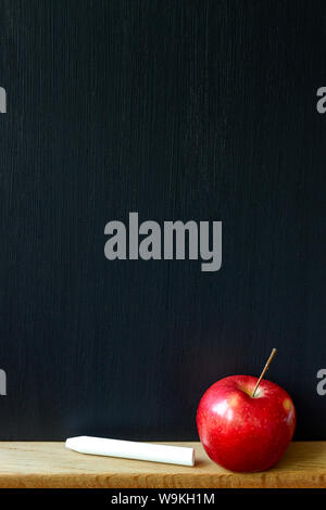 Back to school concept, closeup of a clean black chalk board, white chalk and red apple, selective focus, copy space Stock Photo