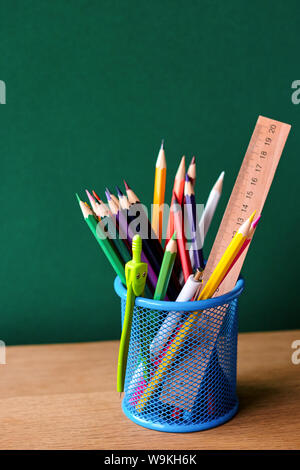 Back to school concept, blue glass with school supplies on a school desk on a background of a clean green chalk board, selective focus, copyspace Stock Photo