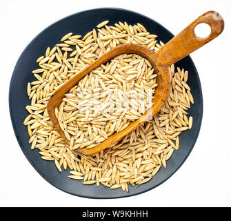 whole, organic oat groats on a rustic wooden scoop against an isolated black plate Stock Photo