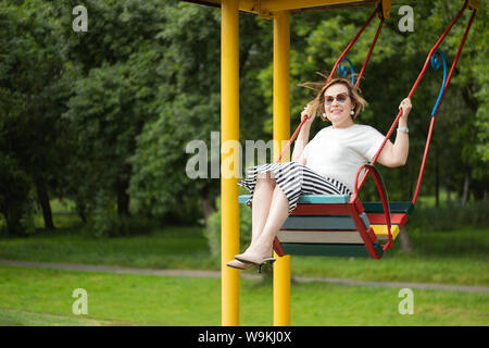Senior mature woman enjoying retirement life feeling happy and healthy having fun swinging on a swing in the park in a sunny beautiful day. Stock Photo