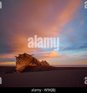 This old shipwreck is stranded for many years. The harsh weather conditions worked on the material.A magical sunset enchants the landscape. Stock Photo