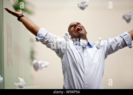 Businessman standing excited with arms raised and mouth open, balls of paper thrown in the air. Stock Photo