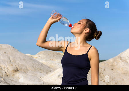 young slender athletic girl drinks water from a plastic bottle after playing sports outdoors Stock Photo