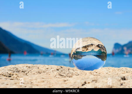 Lake Garda (Lago di Garda or Lago Benaco) seen through a glass crystal  ball placed on rock. Selective focus Stock Photo