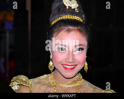 Dressed-up Thai girl wears a golden Lanna-style lace dress and elaborate hairdo with hair jewellery and drop earrings during a rural Yi Peng parade. Stock Photo