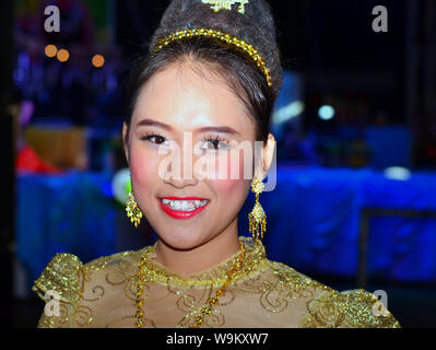 Dressed-up Thai girl wears a golden Lanna-style lace dress and elaborate hairdo with hair jewellery and drop earrings during a rural Yi Peng parade. Stock Photo