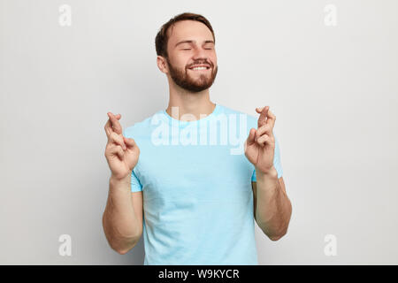 cheerful attractive man wishes luck, desire concept. strong thoughts , close up photo. isolated blue background. willingness Stock Photo