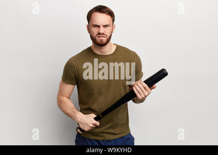 frustrated angry guy holding a bat, looking at the camera, expressing negative emotion. close up photo. isolated white background. studio shot, crime Stock Photo