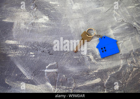 Keys about a charm of the house of blue color on a gray background. Top view. Stock Photo